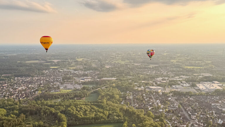 Zwei Heißluftballons schweben bei Sonnenuntergang über Kirchlengern und Herford in Ostwestfalen-Lippe, Ballonfahrt in OWL NRW mit weitem Blick auf Landschaft und Stadt.